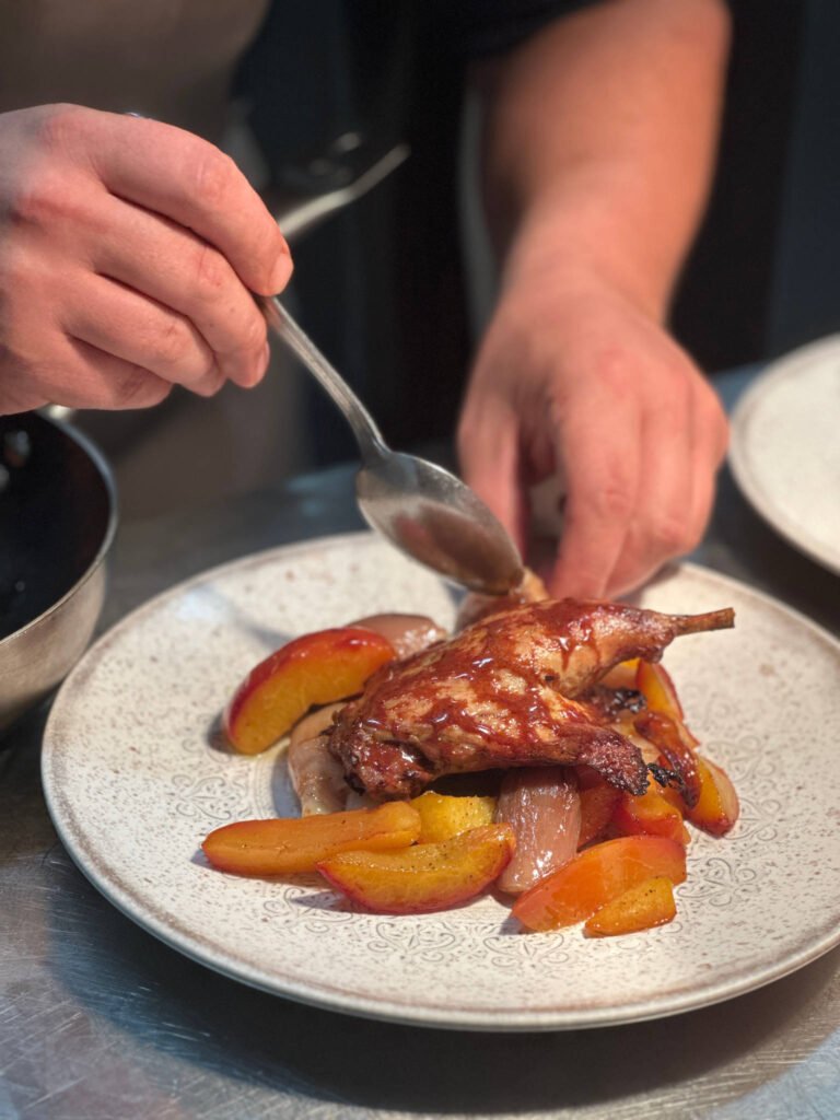 Chef che impiatta coscia d'anatra arrosto con pesche caramellate.