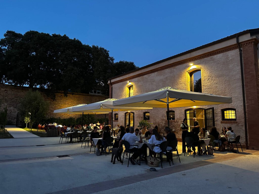 Persone a cena all'aperto sotto grandi ombrelloni bianchi di sera